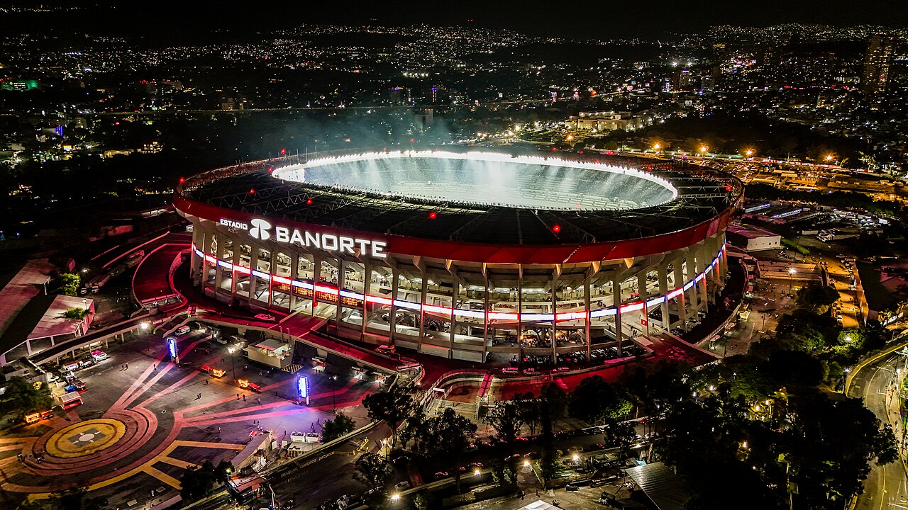 Nächtliche Luftaufnahme des Aztekenstadions in Mexiko-Stadt, vollständig beleuchtet vor dem Hintergrund der Stadt.