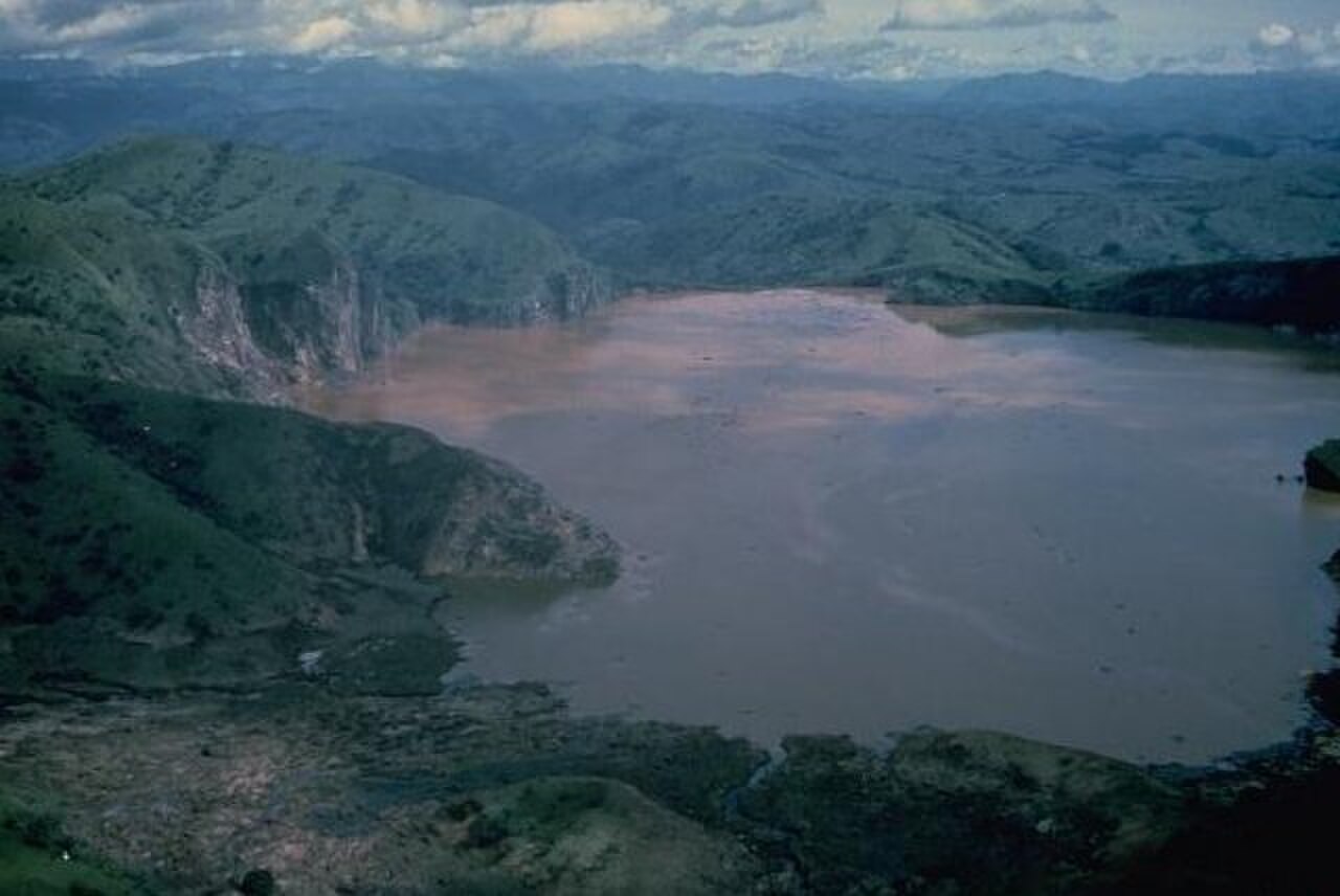 Blick über den Nyos-See in Kamerun, einen Kratersee mit dunkler Wasseroberfläche, umgeben von grünen Berghängen