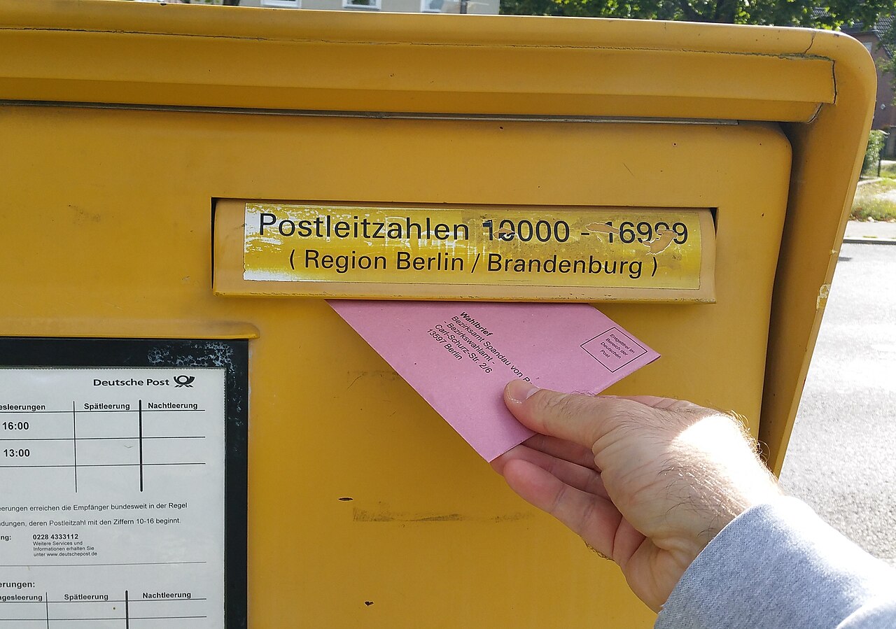 Ein gelber Briefkasten der Deutschen Post, in den ein Wahlbrief zur Bundestagswahl eingeworfen wird.