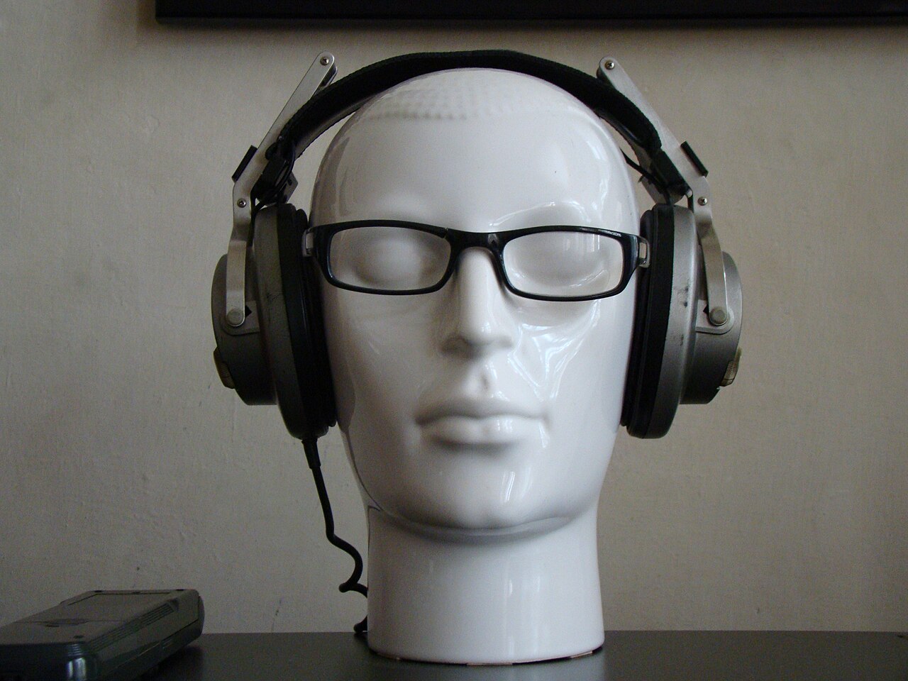 Schwarze Over-Ear-Kopfhörer mit silberfarbenem Bügel, daneben eine Brille auf einer Holzoberfläche.
